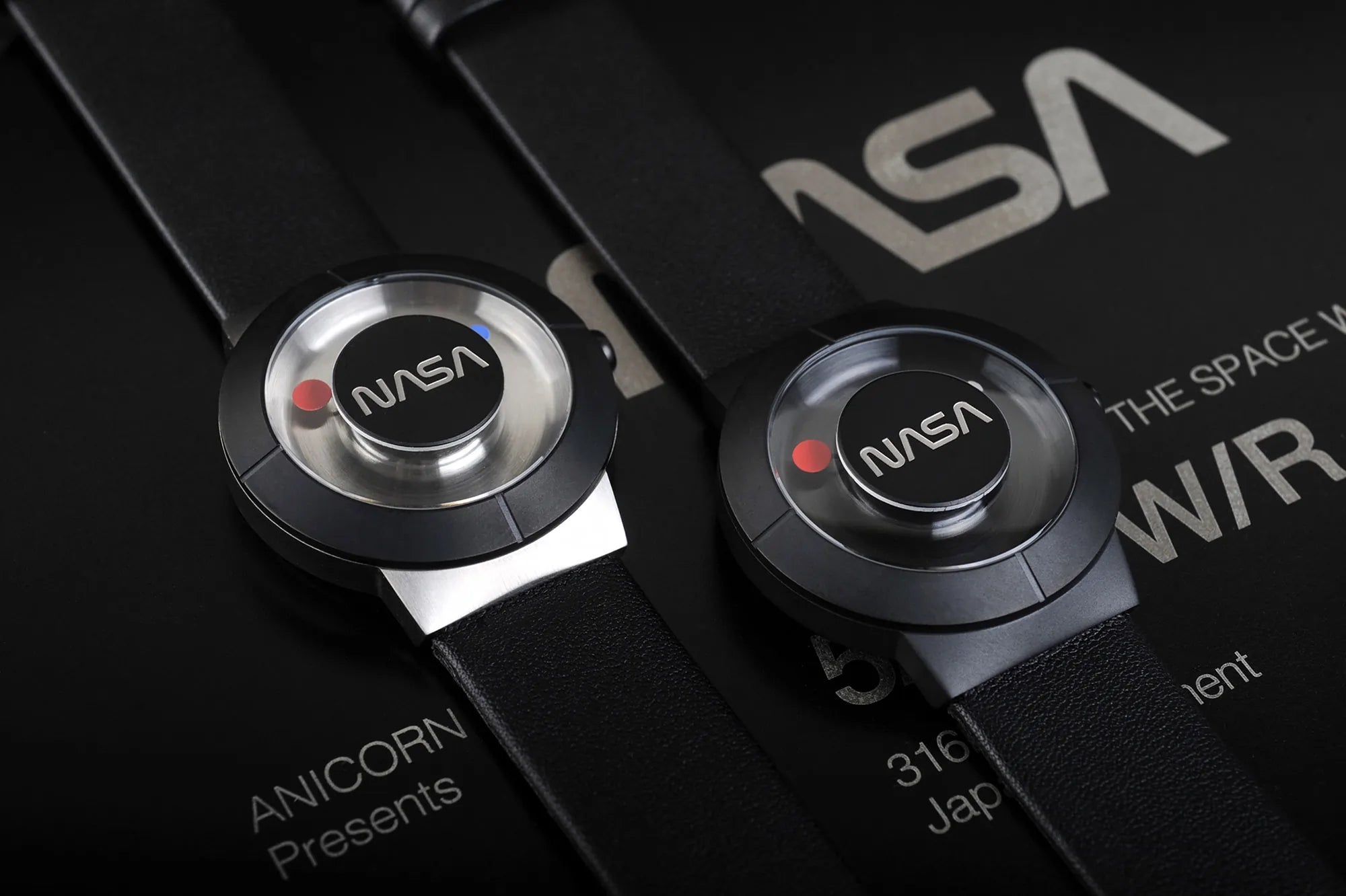 Close-up of two The Space Watch by Richard Danne watches with iconic logo on the dial, resting on premium packaging with subtle branding details