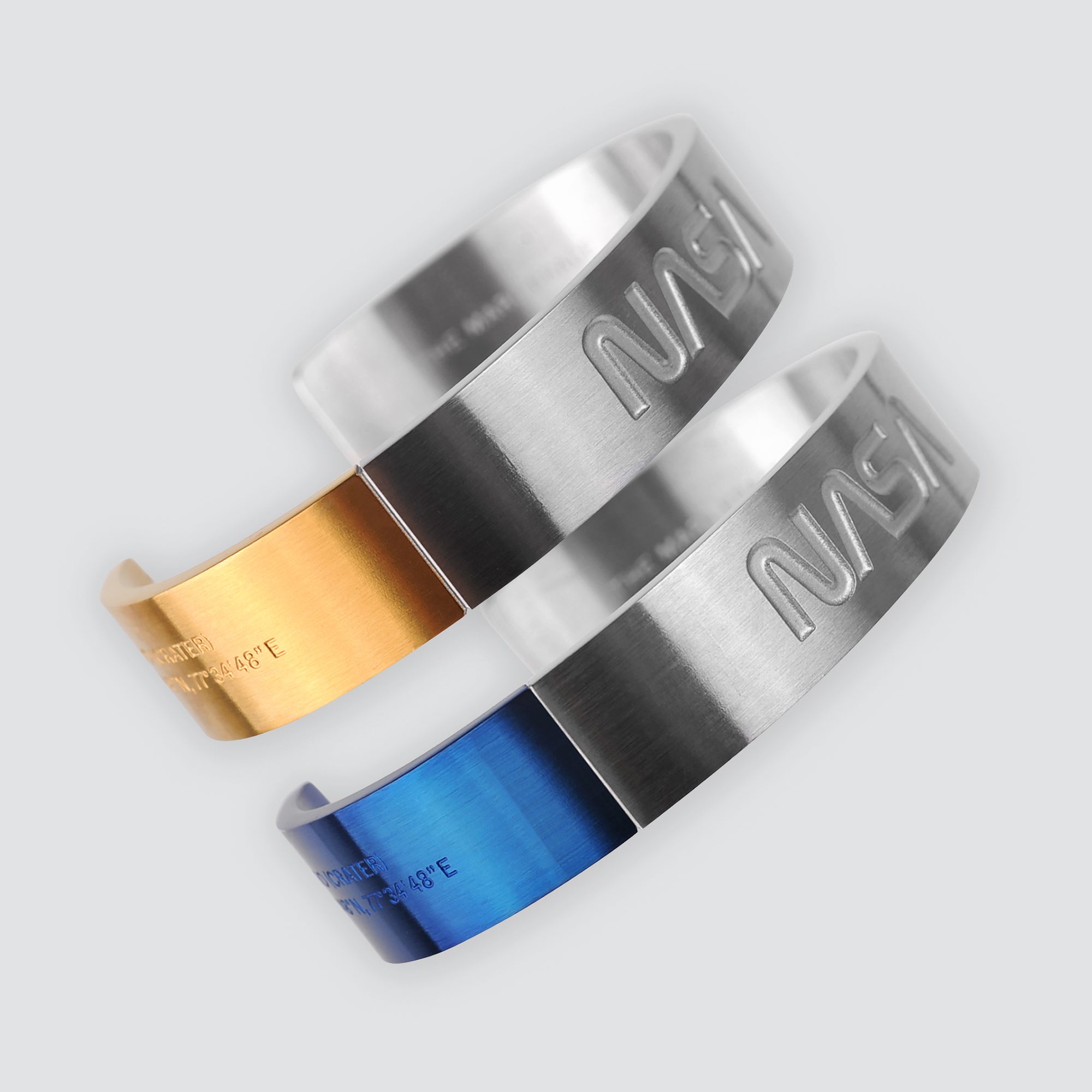 Futuristic elegance. A slip-on gold/silver or blue/silver duo-colored stainless steel bracelet with the landing coordinates and NASA logo embossed. A collaboration with Shannnam.